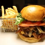 Mushroom burger with bacon on a brioche bun tomatoes lettuce and caramelized onions with basket of fries